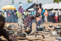 S.Sudanese refugee girl prepares a meal at the camp as others queue for donor food