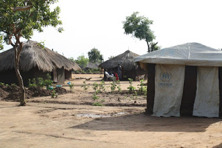 A 30 by 30 plot of land bearing two huts for a family,  a toilet/bathroom and a mall kitchen garden 