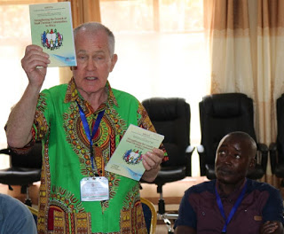 Rev. Fr. Joseph Healey, MM, holding out both the 1st & the 2nd Editions of the Small Christian Community Training Handbooks