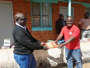 Mr. Diele hands over a book to Fr. Kapiri
